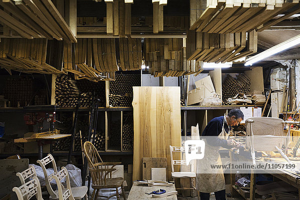 Mann  der an einer Werkbank in einer Schreinerei steht und an einem Holzstuhl arbeitet.