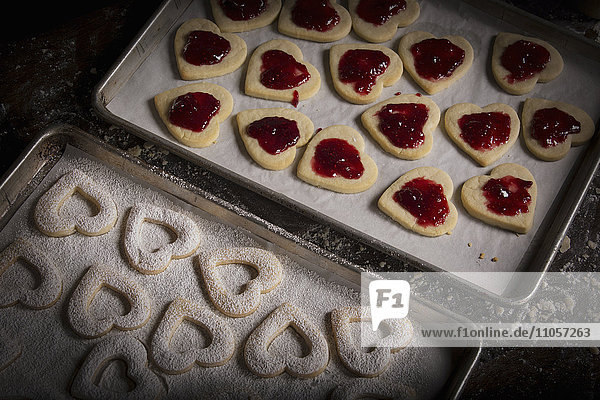 Valentinstag beim Backen  Frau streicht Himbeermarmelade auf herzförmige Kekse.