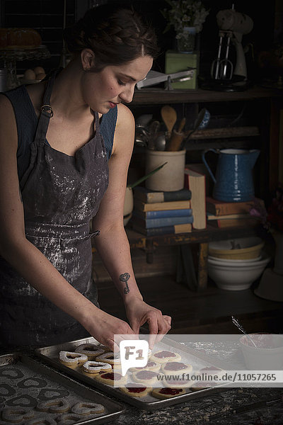 Valentinstag beim Backen  junge Frau steht in einer Küche  mit einem Backblech mit herzförmigem Keks.