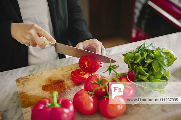 Eine Frau schneidet mit einem scharfen Messer Tomaten in Scheiben.