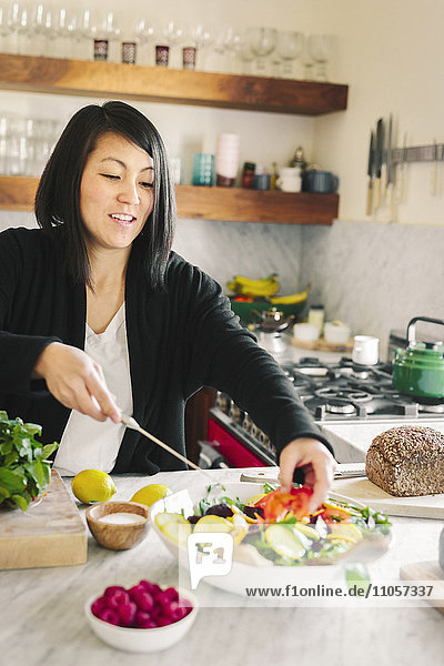 Eine Frau in einer Küche  die ein Salatgericht mit frischem Gemüse zubereitet.