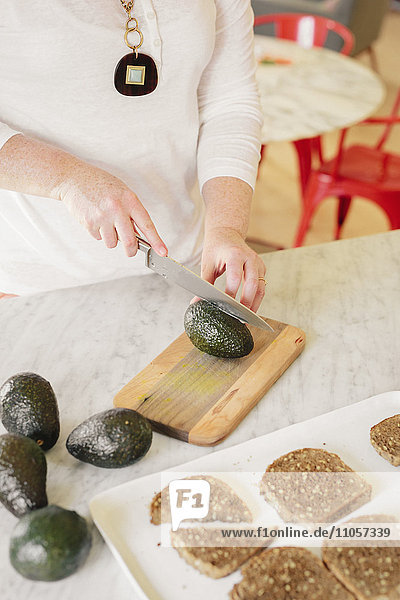 Eine Frau schneidet eine Avocado in Scheiben  um offene Sandwiches zu machen.