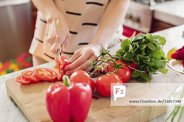 Eine Person an einer Küchentheke  die Salat zubereitet und frische Tomaten schneidet.