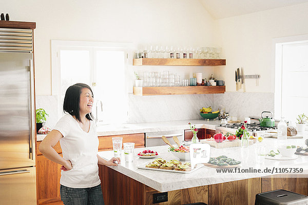 A woman in a kitchen by a counter with prepared salads and food dishes.