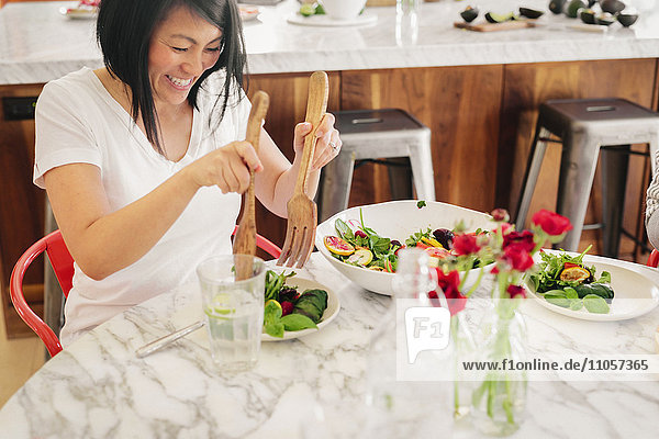 A woman using salad servers to load her plate with fresh salad leaves.