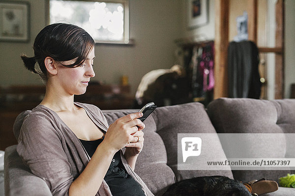 A woman on the sofa using her smart phone to text.