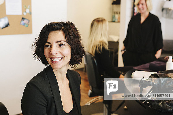 A client sitting at a hair salon  with two people in the background.