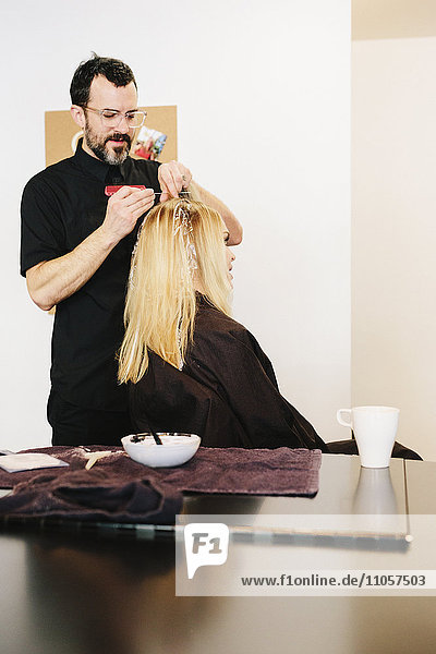 Eine Haarkoloristin  die mit Folien arbeitet  um einer Kundin mit langen blonden Haaren mit Hilfe von Farbe Highlights und Lowlights zu geben.