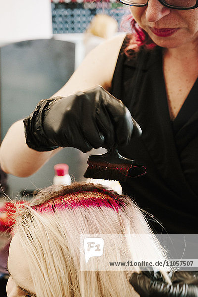 Ein Haarkolorist mit Handschuhen  der mit einer Bürste rote Haarfarbe auf das blonde Haar eines Kunden aufträgt.