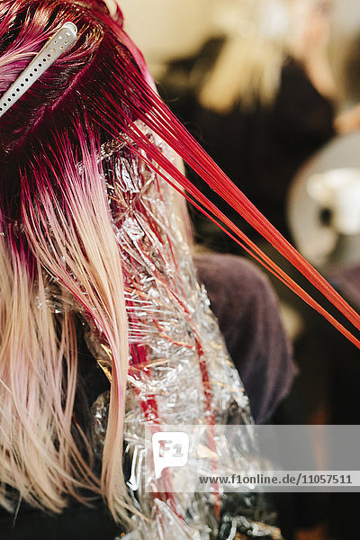 Ein Haarkolorist  der die rosa Haarfarbe auf das lange blonde Haar einer Kundin aufträgt.