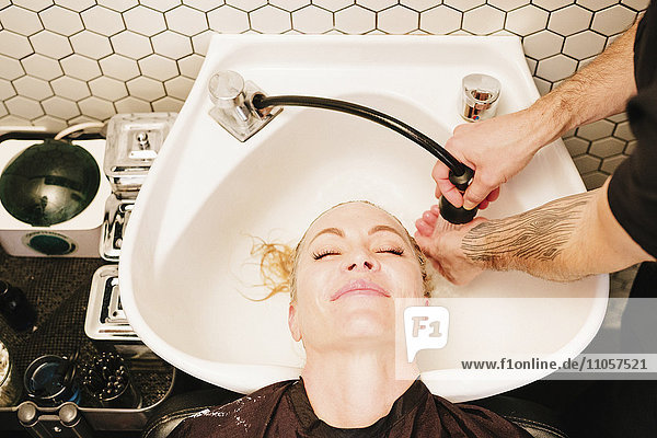 Eine Kundin in einem Friseursalon  die sich in einem Becken die Haare spülen lässt.