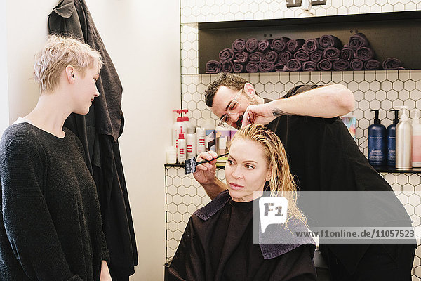 Ein Friseur  der in einem Friseursalon einer Frau die Haare schneidet.