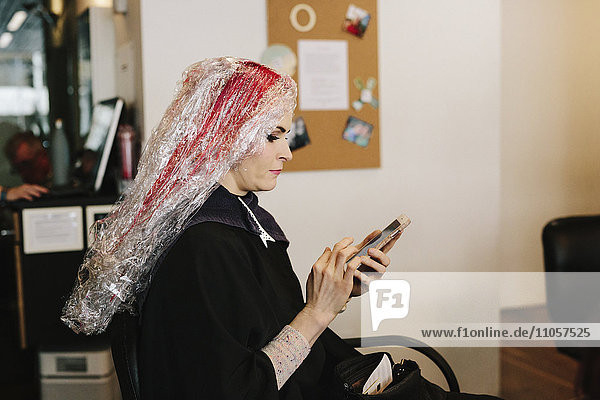 Eine Frau in einem Friseursalon bei einer Haarfarbenbehandlung  die ein Smartphone benutzt.