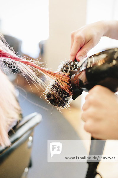 Ein Friseur föhnt das lange glatte rosa Haar eines Kunden mit einer Rundborstenbürste.