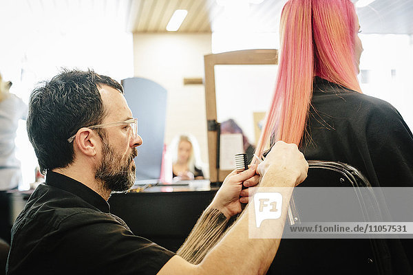 Eine Friseurin schneidet zusammen mit einer Kundin die Enden ihrer langen  rosa gefärbten  glatten Haare.