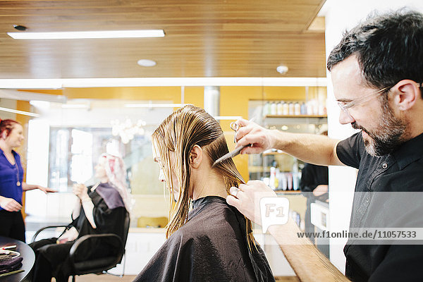 A hair stylist with a client  combing her long hair in sections.