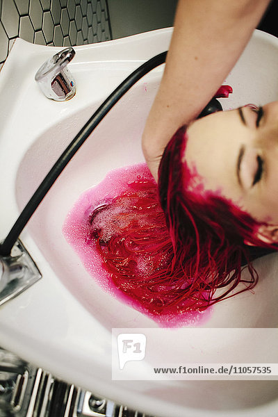 Eine Kundin eines Friseursalons lässt sich über einem Becken rote Haarfarbe aus den Haaren spülen.