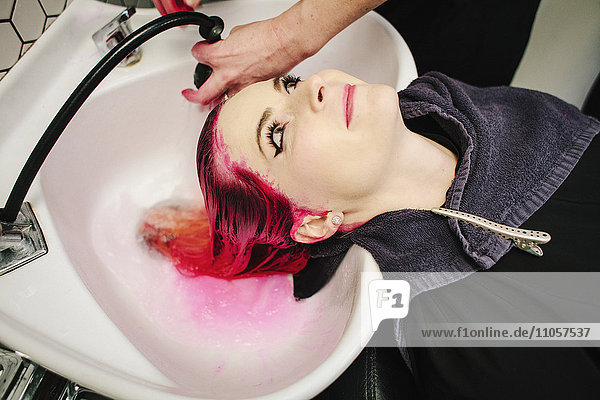 Eine Frau  deren Haare mit rotem Farbstoff gespült werden  läuft in das Becken.
