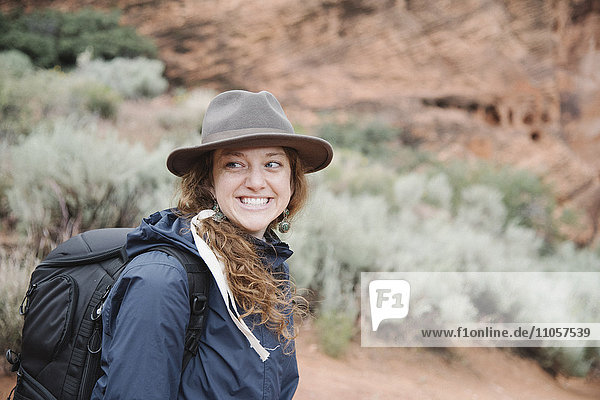 Smiling woman with auburn hair  wearing a hat and carrying a backpack  hiking in a canyon.