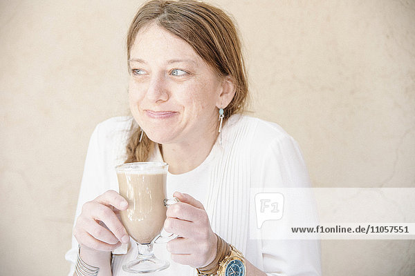 Portrait of a smiling woman with auburn hair holding a cafe latte.