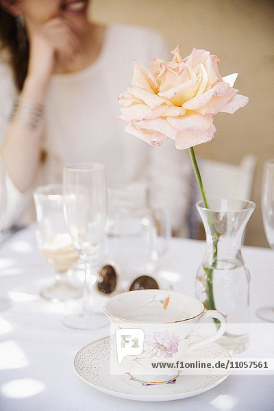 Nahaufnahme einer Rose in einer Vase auf einem Tisch mit einer Tasse und Untertasse und Gläsern.