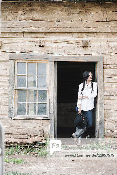 Junge Frau mit langen braunen Haaren in Zöpfen  die in der Türöffnung einer Holzhütte steht.