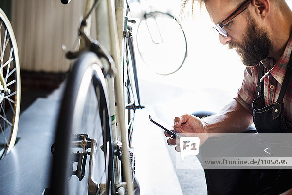Ein Fahrradmechaniker in einer Fahrradwerkstatt mit einem Smartphone.