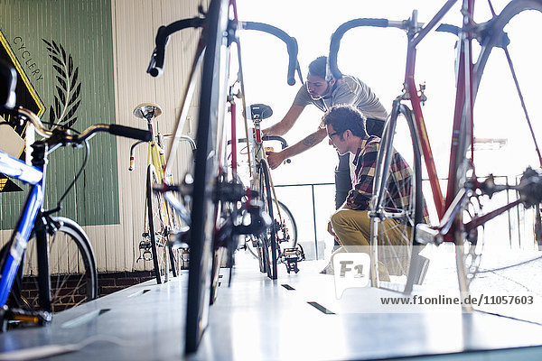 Ein Mann  der in einer Fahrradwerkstatt arbeitet und zusammen mit einem Kunden ein Fahrrad überprüft.