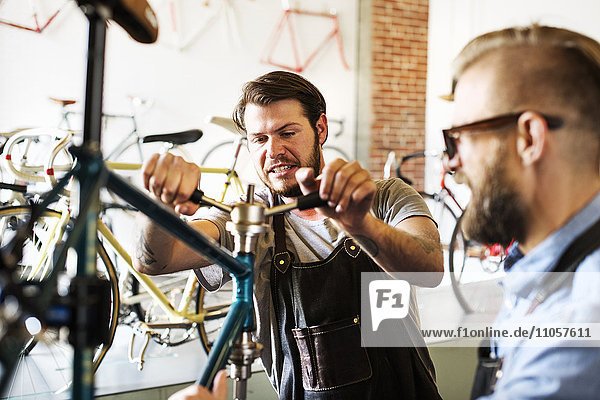 Two men in a cycle repair shop  looking at a bicycle.