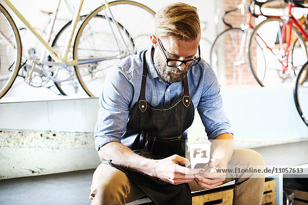 Ein Mann  der in einer Fahrradwerkstatt arbeitet und sein Telefon auf Nachrichten überprüft. Kaffeepause.