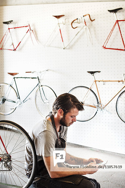 Ein Mann  der in einer Fahrradwerkstatt arbeitet und mit seinem Smartphone sitzt.