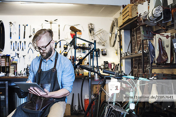 A man working in a bicycle repair shop seated using a digital tablet.