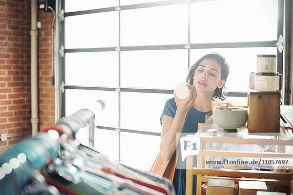 Junge Frau in einem Geschäft  die einen Keramikbecher betrachtet.