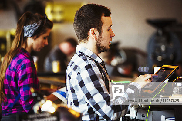 Spezialisiertes Kaffeehaus. Eine Frau und ein Mann arbeiten hinter der Theke an einer Röstmaschine.