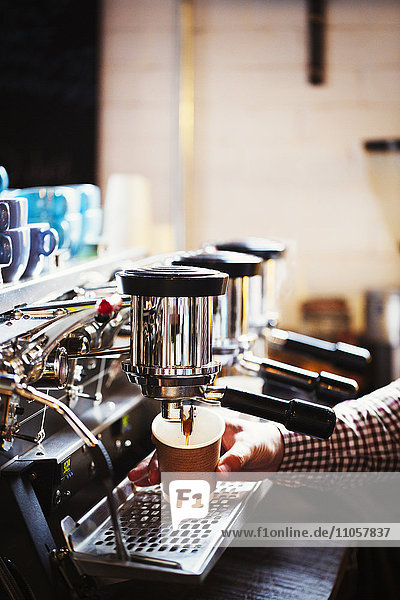 Spezialisiertes Kaffeehaus. Eine Person  die an einer großen Kaffeemaschine arbeitet  mit drei Spendern für perkolierenden Kaffee  Griffen und einem Rohr  das Dampf abgibt.