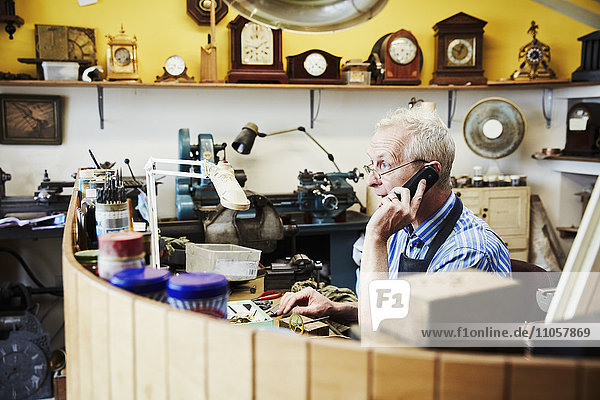 Ein Uhrmacher am Telefon in seiner Werkstatt.