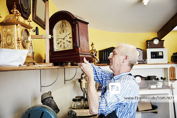 Ein Uhrmacher  der sein Werk auf einem Regal in seiner Werkstatt ausstellt.