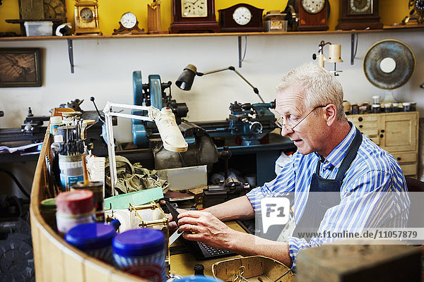 Uhrmacher in seiner Werkstatt mit einem Laptop.