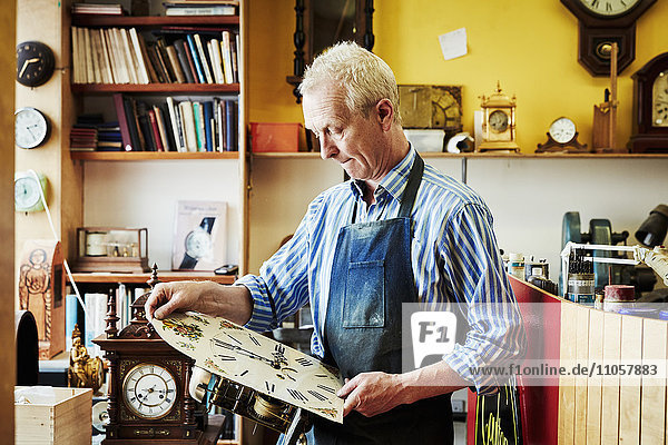 Ein Uhrmacher  der seine Arbeit in der Werkstatt betrachtet.