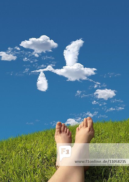 Frau liegt auf Wiese Detail Füße Himmel Wolkenformation in Form eines Storches der ein Baby in einer Windel bringt