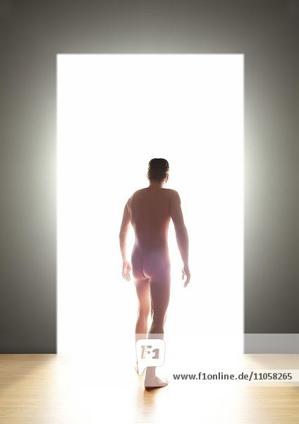 Nackter junger Mann Rückenansicht geht durch eine Tür ins Licht