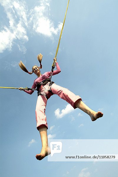 Junge Frau springt an Seilen auf Bungee-Trampolin