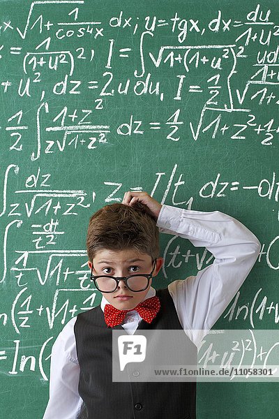 Ratloser Schuljunge mit Brille und Fliege vor Schultafel mit mathematischen Gleichungen