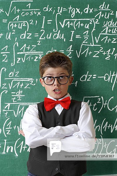 Schuljunge mit Brille und Fliege vor Schultafel mit mathematischen Gleichungen