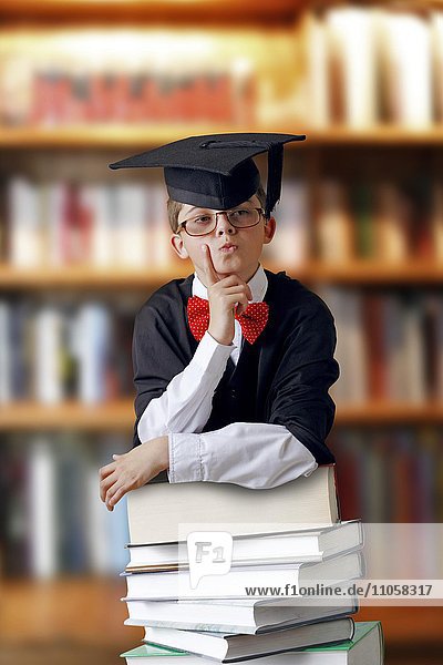 Nachdenklicher Schuljunge mit Doktorhut und Bücherstapel in Bücherei
