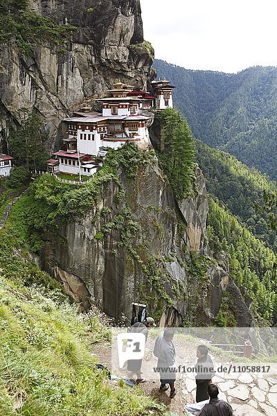 Tigernest-Kloster an der Felswand des Paro-Tals  vorne Männer in Gho Tracht  Taktshang Goemba  bei Paro  Himalaja  Königreich Bhutan