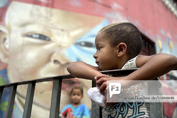 Junge vor dem Graffiti eines Baby-Gesichts  Favela im Distrikt Sapopemba  Zona Sudeste  Sao Paulo  Brasilien  Südamerika