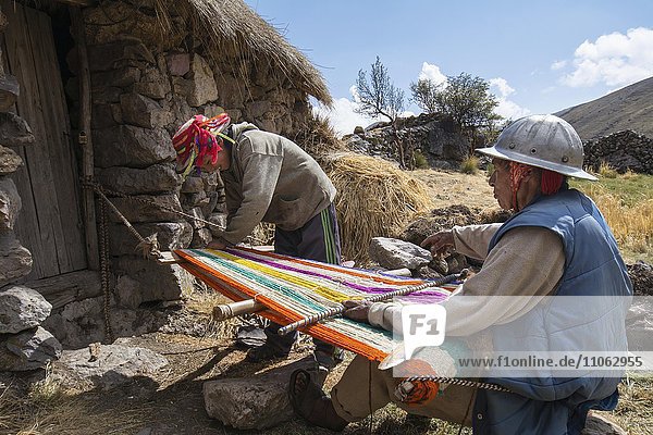 Alter Indio Mann mit Helm webt einen bunten Teppich mit einfachen Webrahmen  bei Cusco  Peru  Südamerika