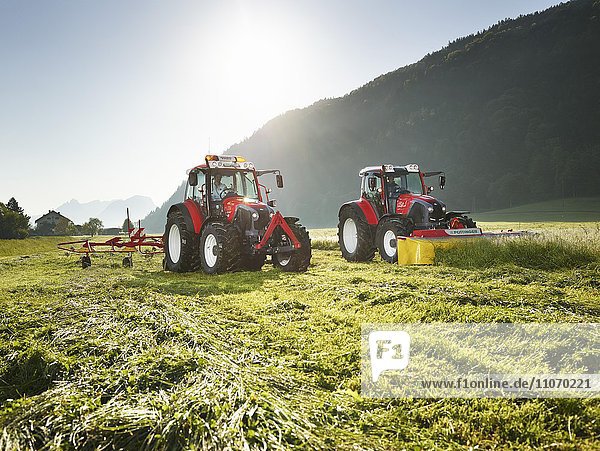 Zwei Traktoren mähen und verteilen das geschnittene Gras mit einem Heuwender  Kundl  Inntal  Tirol  Österreich  Europa