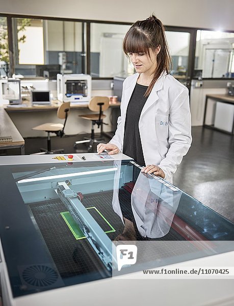 Technikerin  Frau 20-25 Jahre  mit weißem Laborkittel bedient einen Laser Cutter in einem Elektronik Labor  Wattens  Innsbrucker Land  Tirol  Österreich  Europa